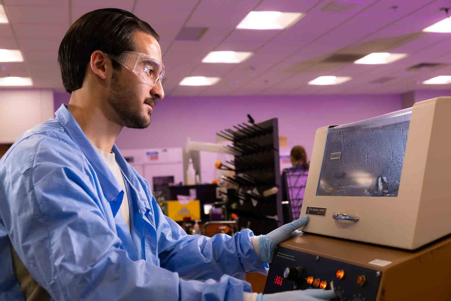 Healthcare professional in scrubs uses vintage computer equipment in a room with pink lighting.