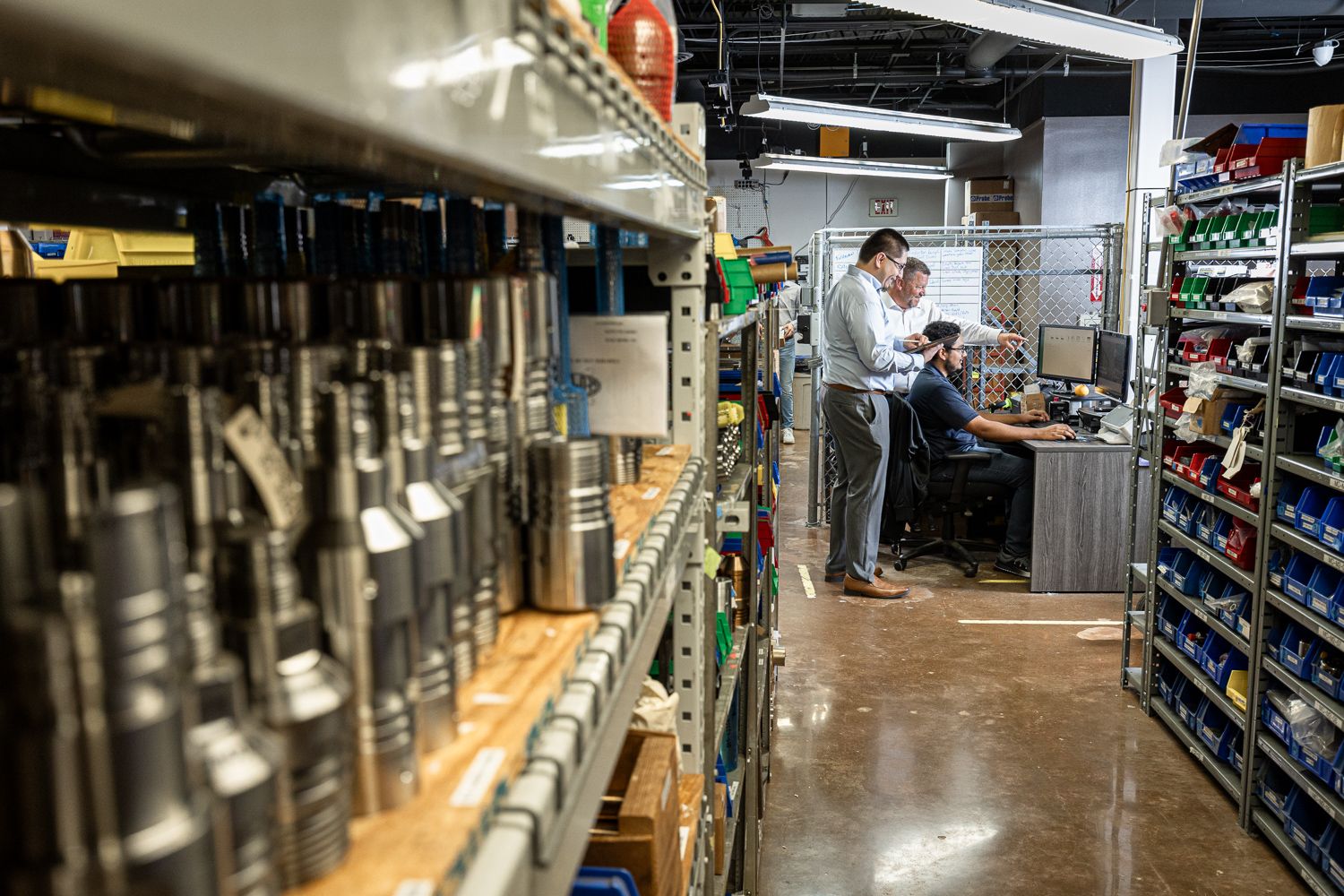 Inside a warehouse, someone checks inventory between shelves stocked with industrial parts and equipment.