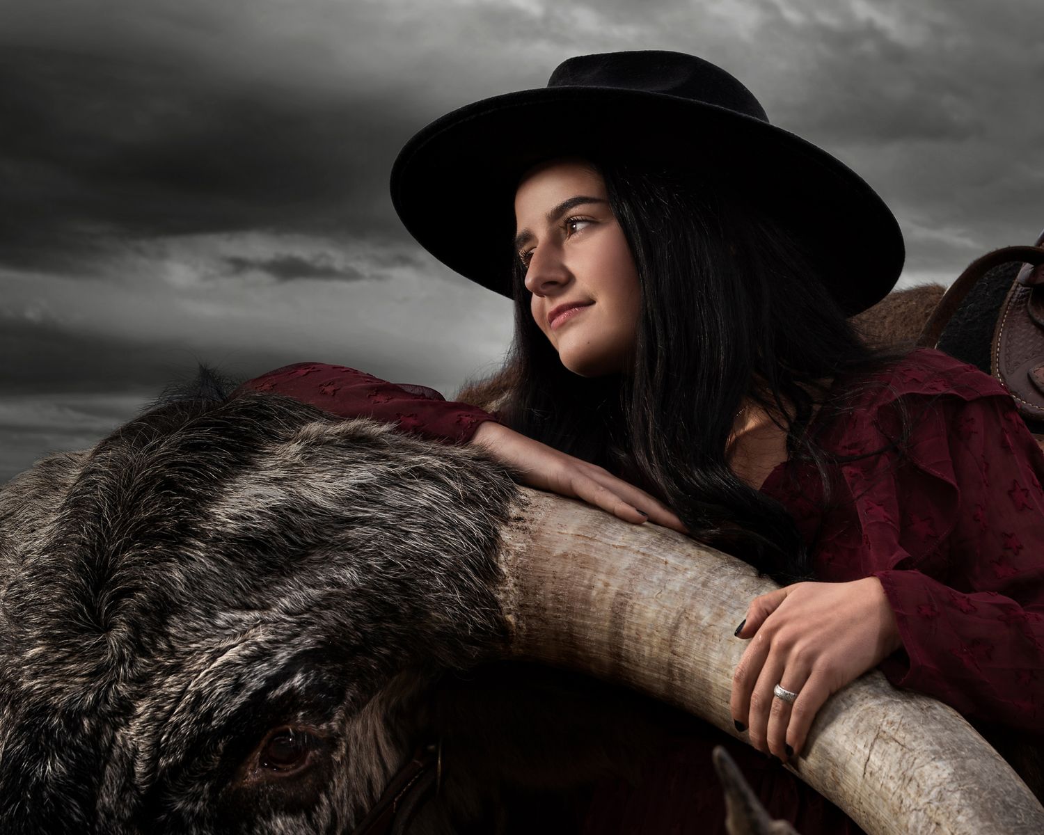 Dramatic black and white photo of person in hat leaning on rustic fence post.