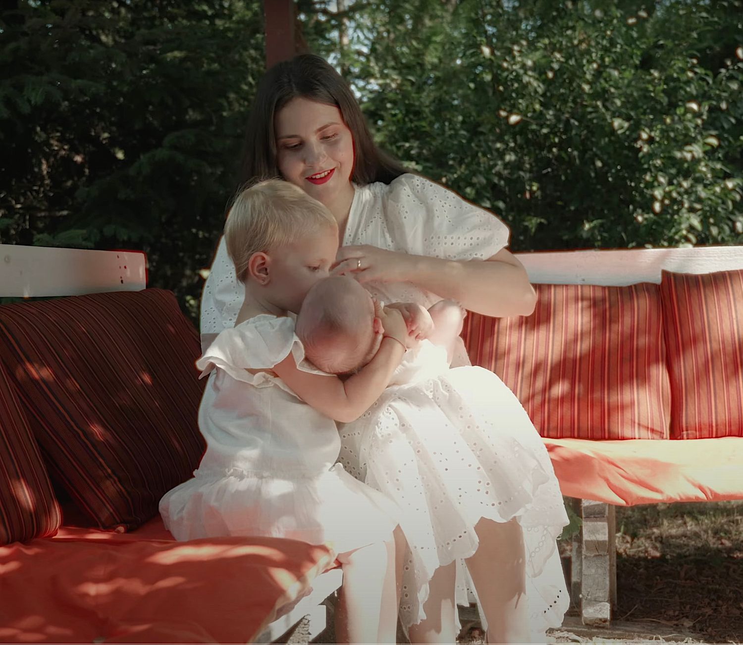 Mother holding a baby next to a smiling child during a baptism ceremony