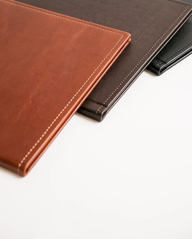Stacked genuine leather photo albums in tan and dark brown finishes.