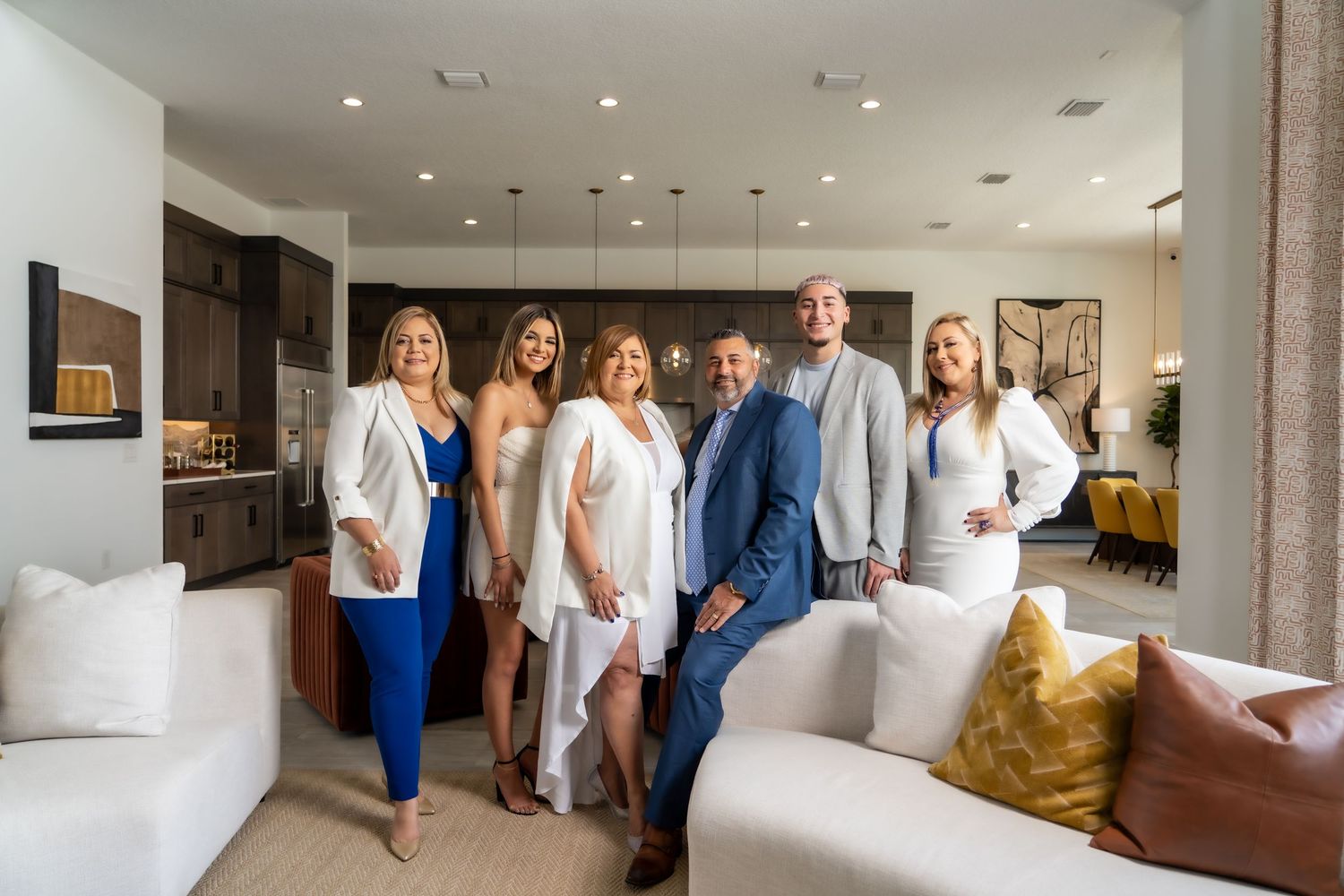 A group stands together in a modern living room with white furniture and yellow accent pillows.