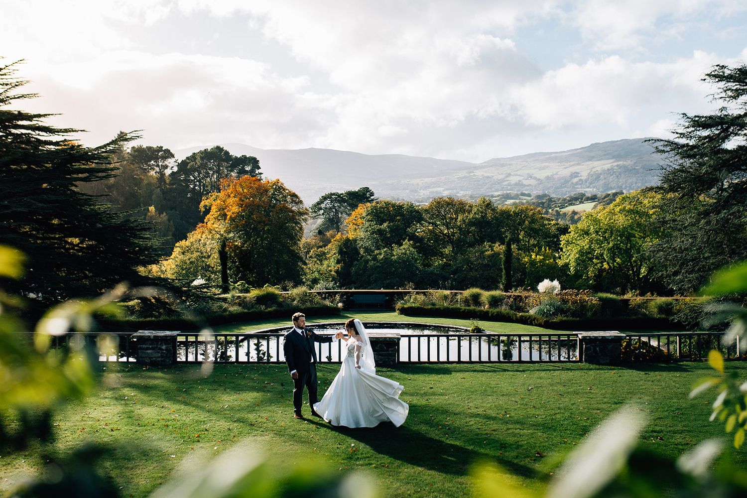 Rolling hills and mountains provide a scenic backdrop to a white building nestled among lush green grounds.