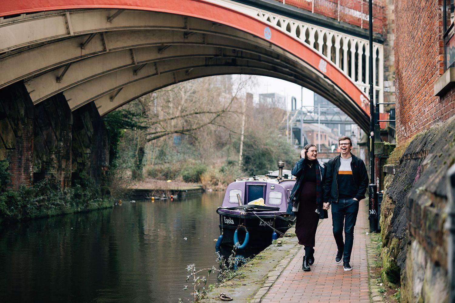 A series of brick railway arches and tunnels with pedestrians walking along a canal path in an urban setting.