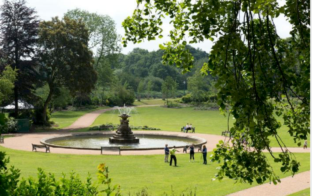 A scenic panoramic view of a peaceful public park with winding paths, lush trees, and people enjoying outdoor activities.