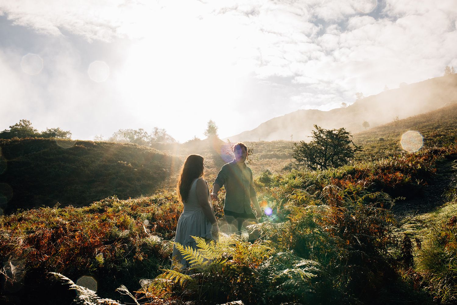 Silhouettes of people enjoying a scenic mountain sunset with lens flare and golden light streaming through clouds.