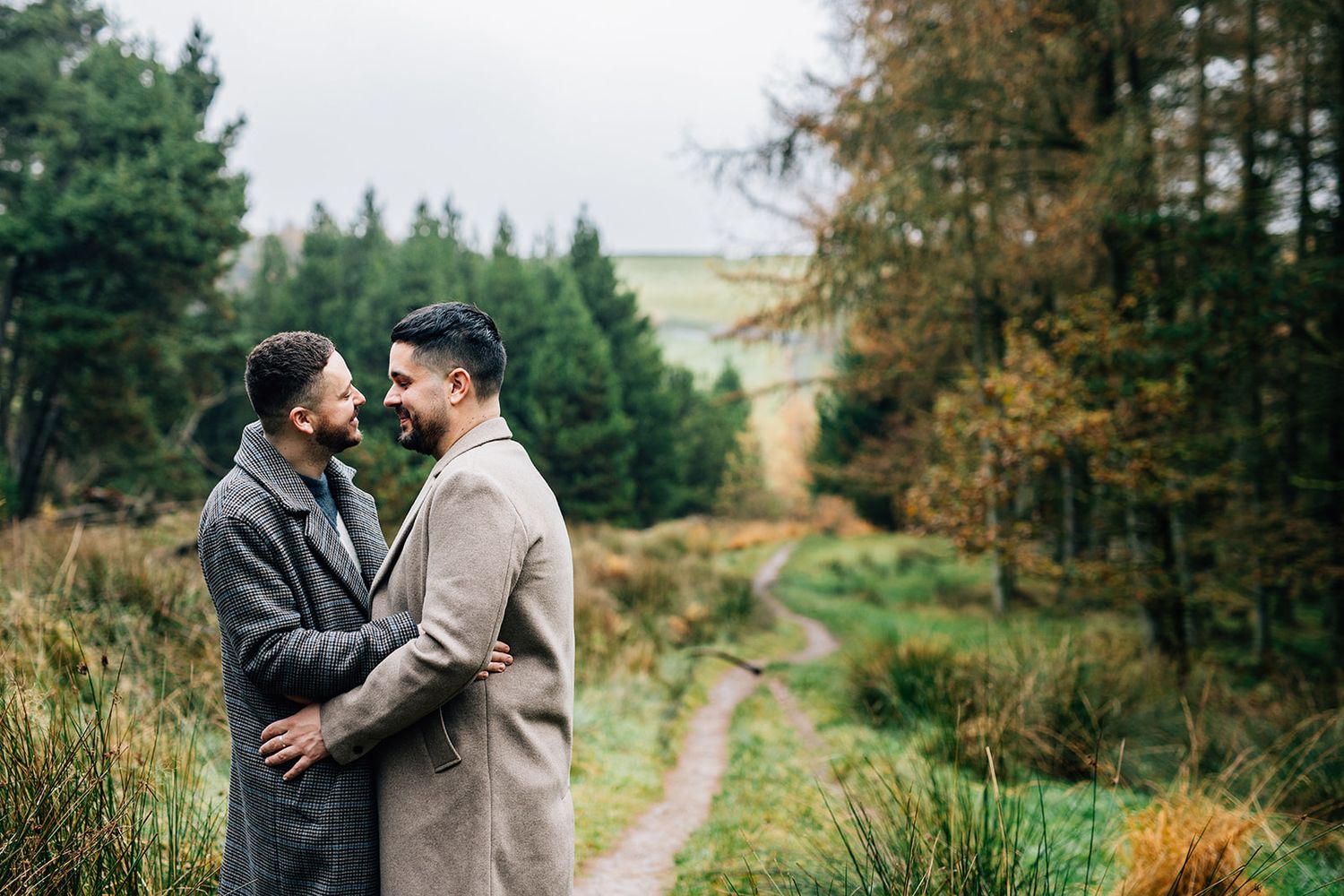 Romantic couple embraces on a scenic mountain trail surrounded by evergreen trees and misty landscapes.