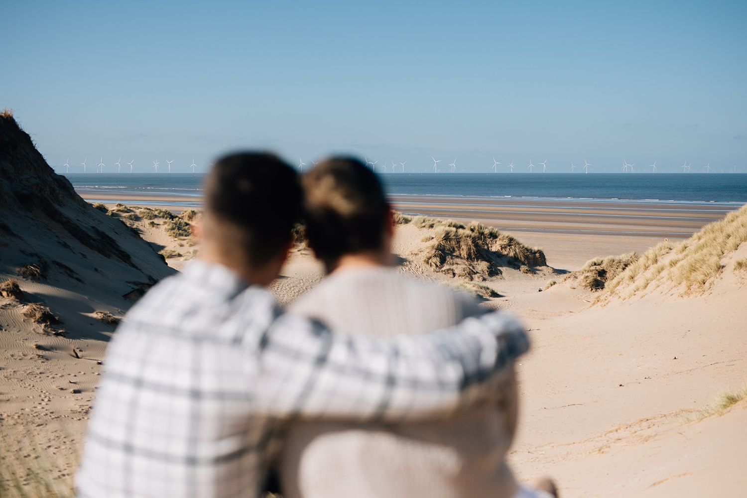Two people walking together on a scenic beach with sand dunes and ocean views on a sunny day.