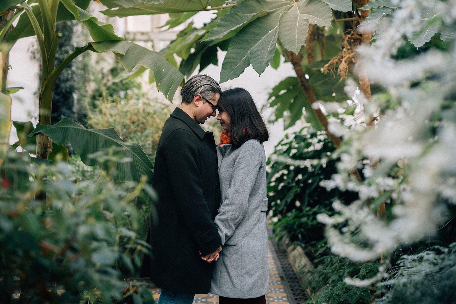 A couple shares an intimate moment together in a lush green outdoor setting during a photo session.