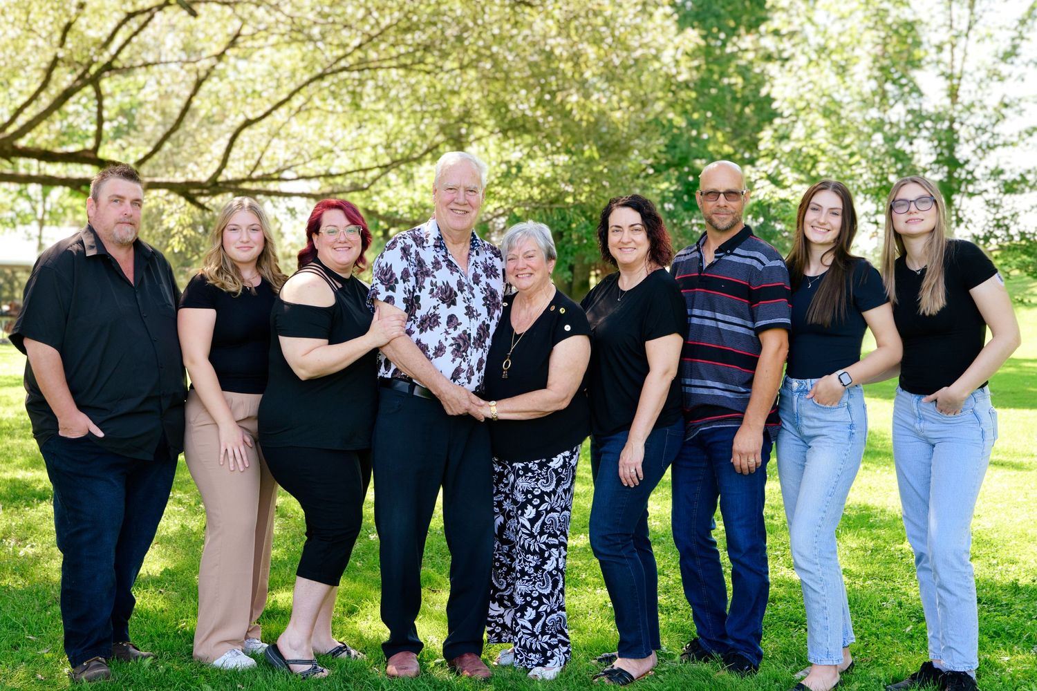 Group of people standing together outdoors in casual attire against a green nature background.
