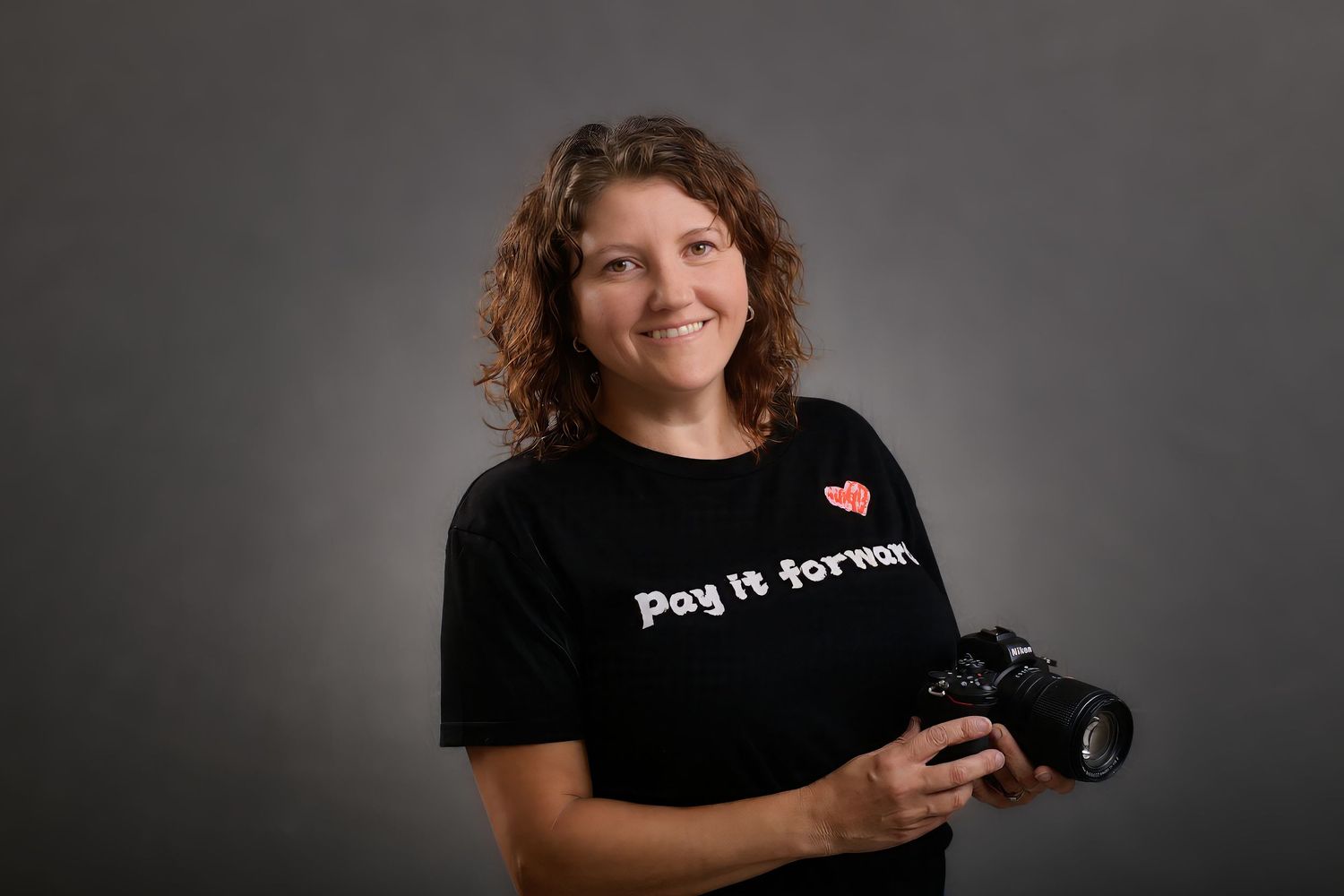 Professional photographer wearing a black t-shirt holds a DSLR camera in a studio setting.