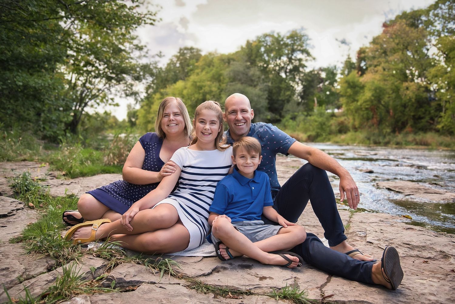 People sitting together on rocky terrain near a river during an outdoor family photo session.