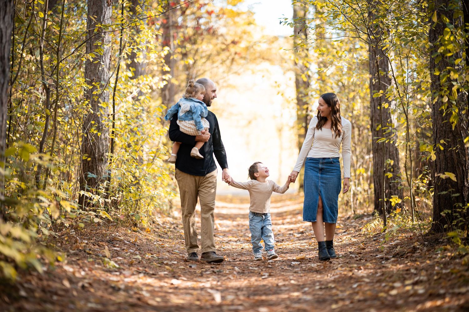 Family walking together on a sunlit autumn forest trail holding hands during golden hour.
