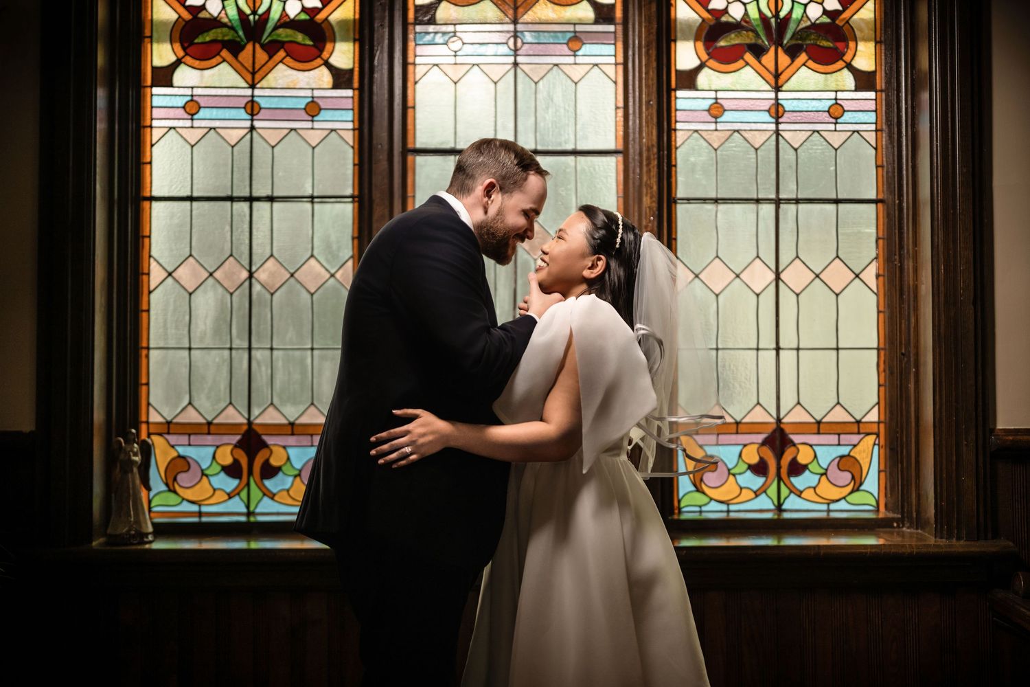 Bride and groom share a romantic moment in front of stunning stained glass windows in a historic church.