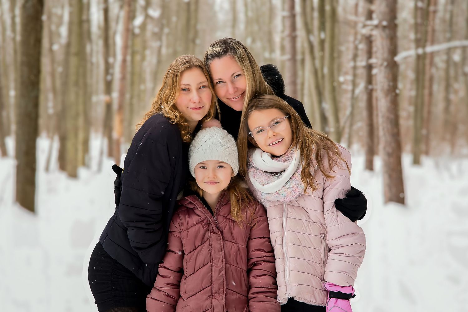 A family group poses together outdoors in a snowy winter forest setting wearing warm coats and winter attire.