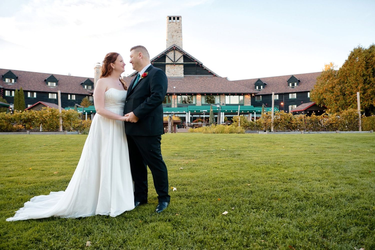 Bride and groom share a romantic moment on green lawn before a large elegant lodge venue on their wedding day.