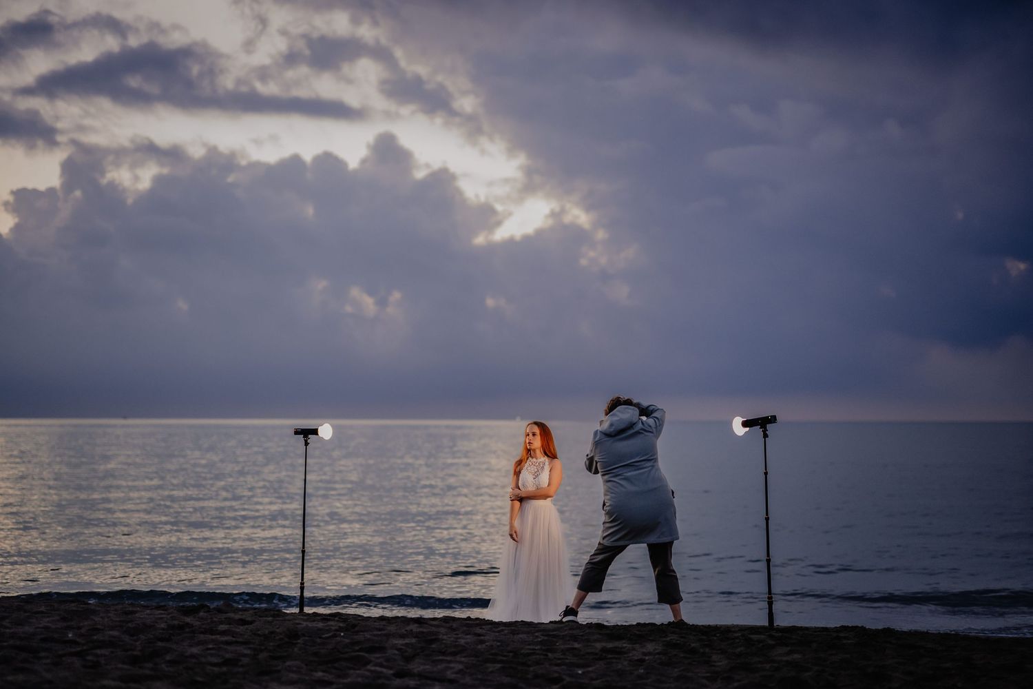 A photographer captures a sunset beach photo session with dramatic storm clouds over the ocean.