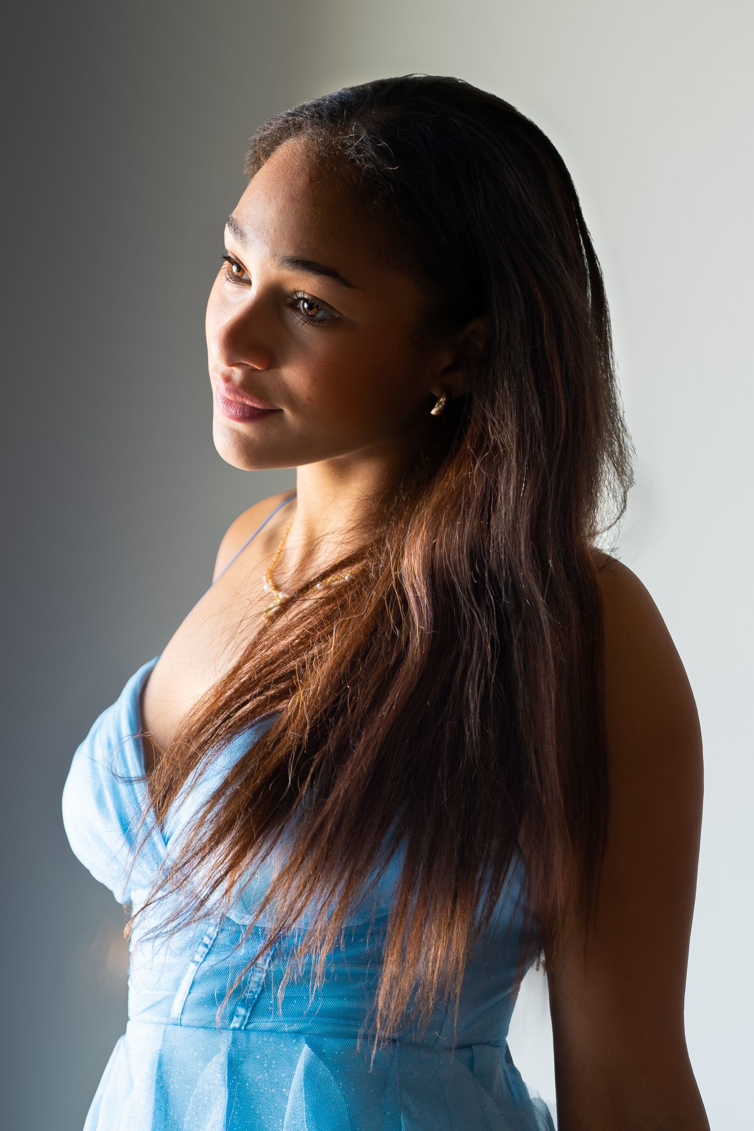 Young Black woman with long hair wearing a blue dress poses for a portrait against a gray background.