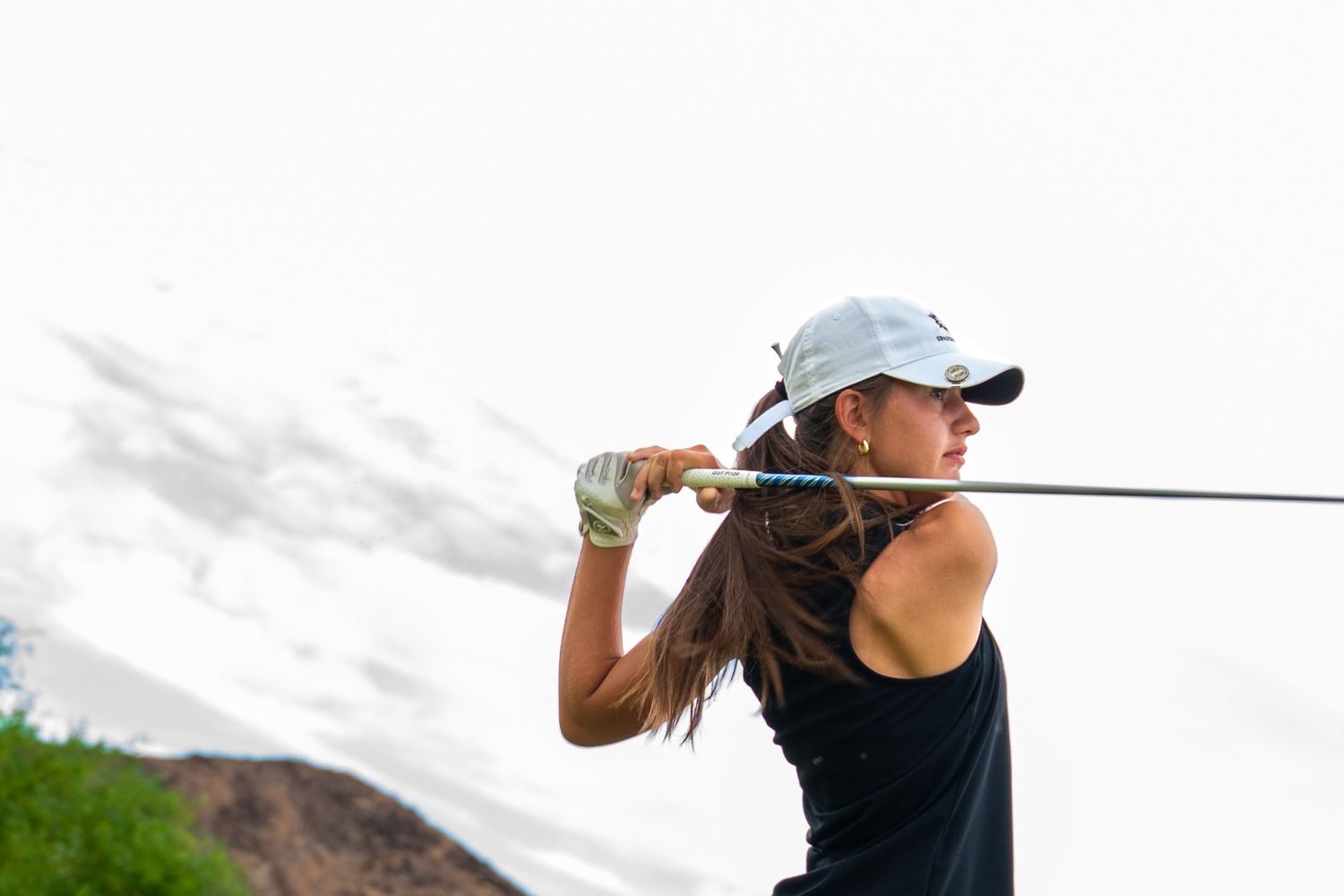 Female golfer follows through on a swing with a golf club against an overcast sky background.