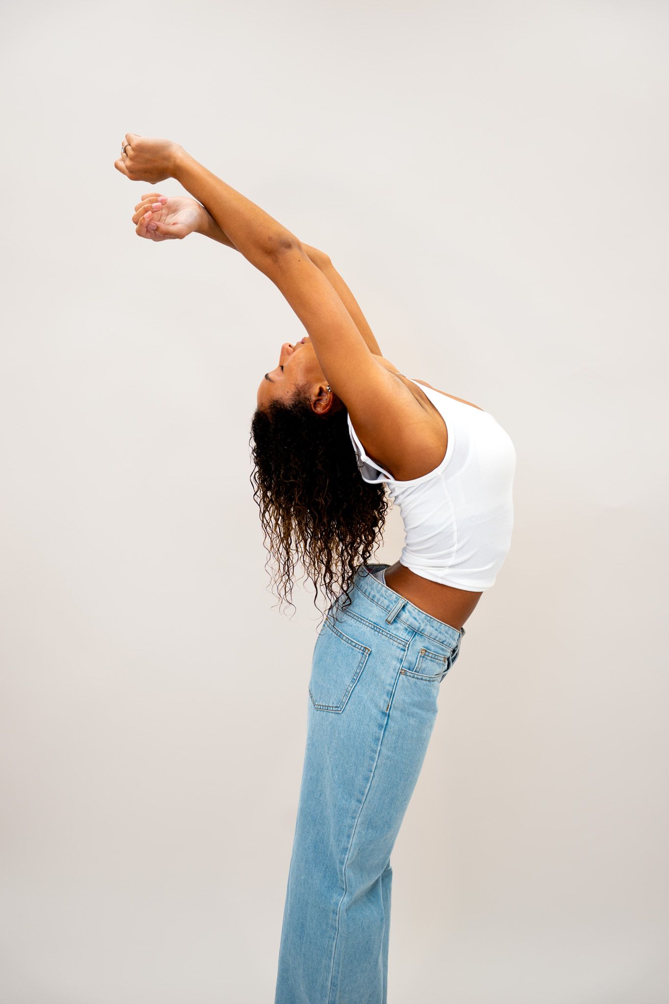 Woman in white crop top and jeans performing a dramatic backbend stretch against white background.