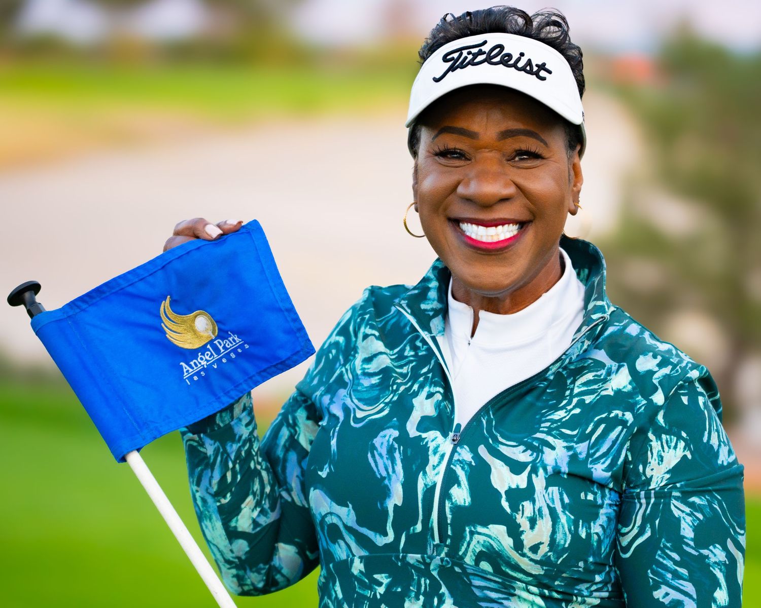 Happy woman in teal Titleist golf attire holds blue tournament flag outdoors.