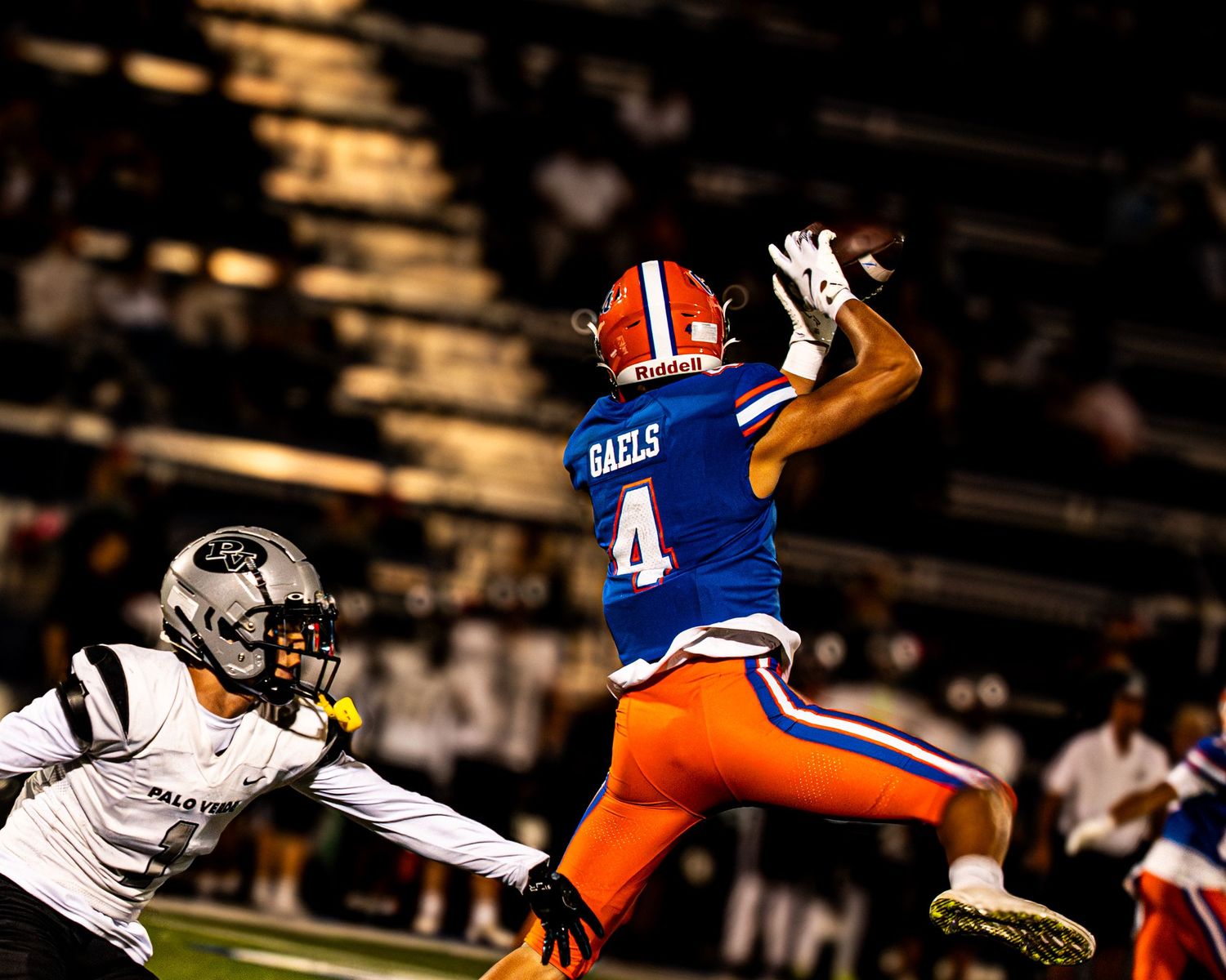 Football player wearing number 4 Gaels jersey leaps to catch a pass during a night game.