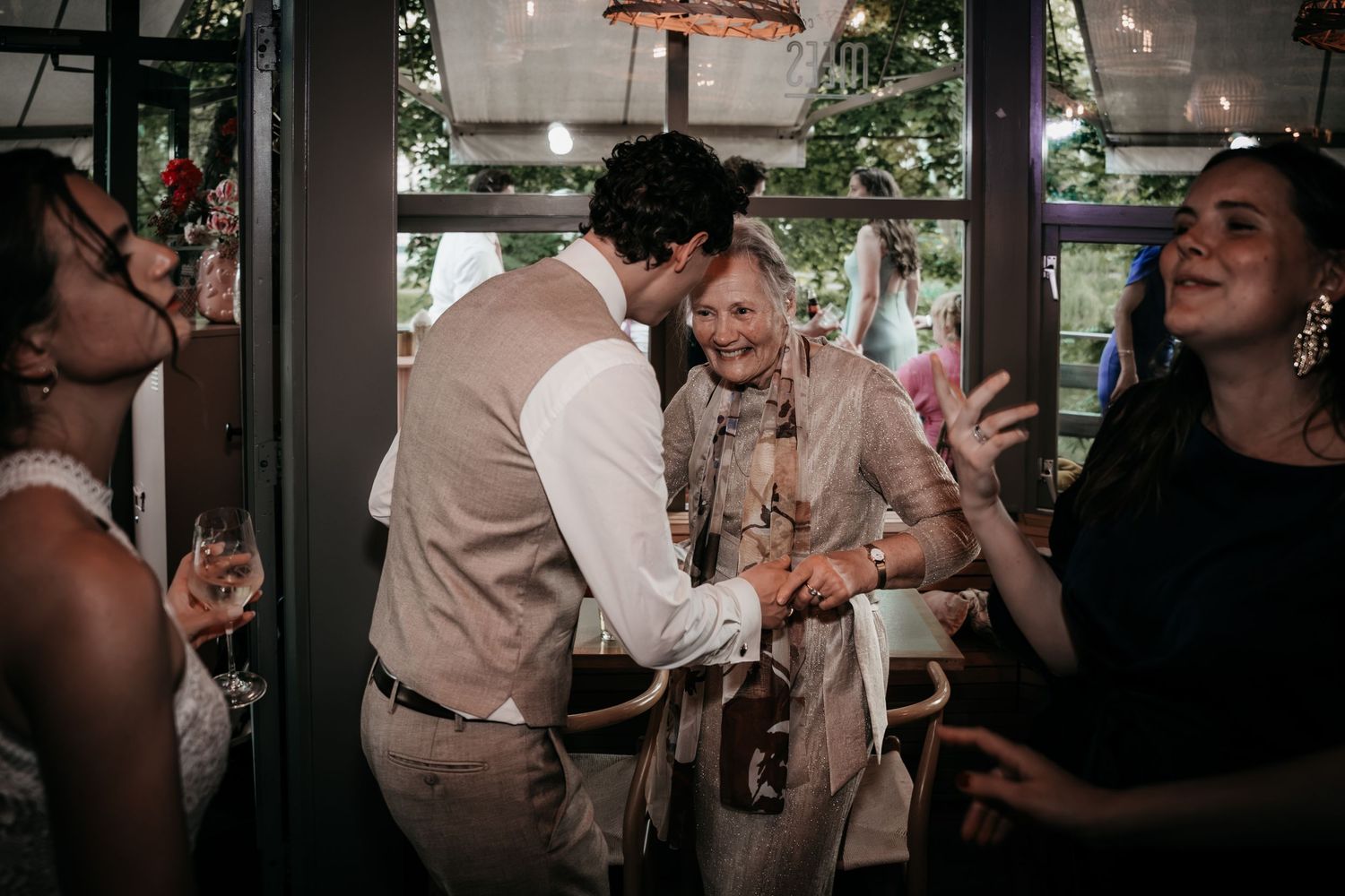 Groom warmly greeting elderly female wedding guest while bride stands nearby at reception.