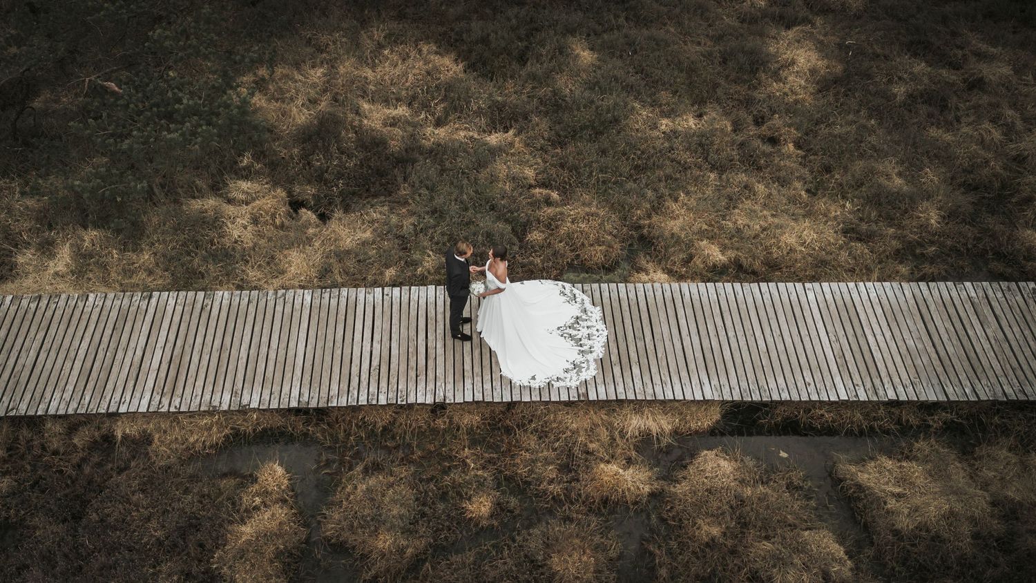 Aerial view of bride and groom embracing on a wooden boardwalk surrounded by moorland.
