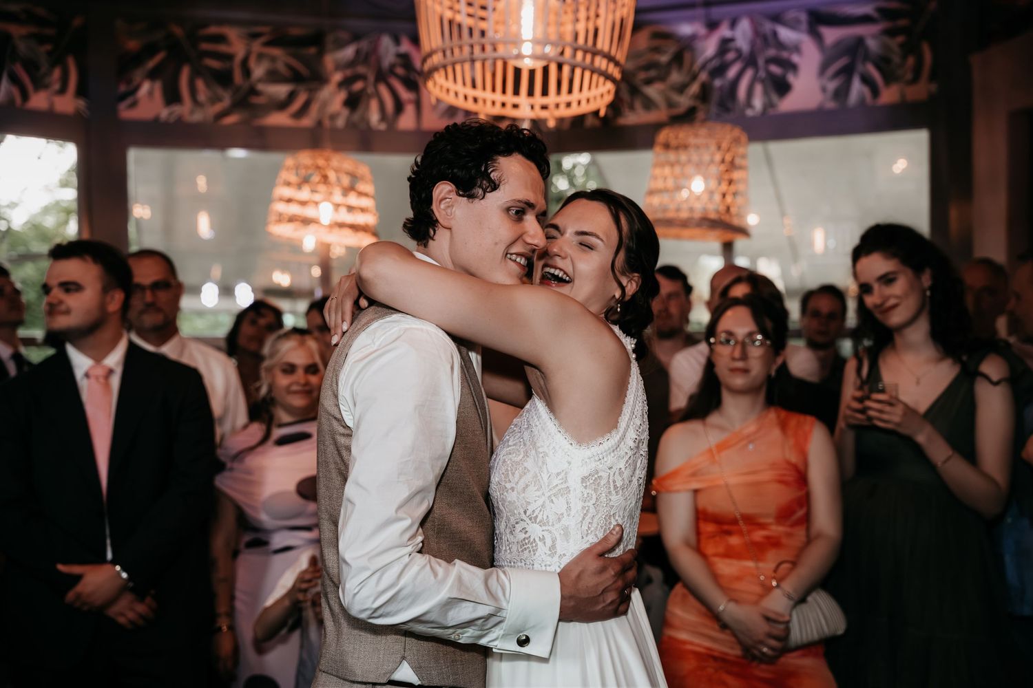 Newlyweds sharing a warm embrace during first dance while wedding guests watch and smile.