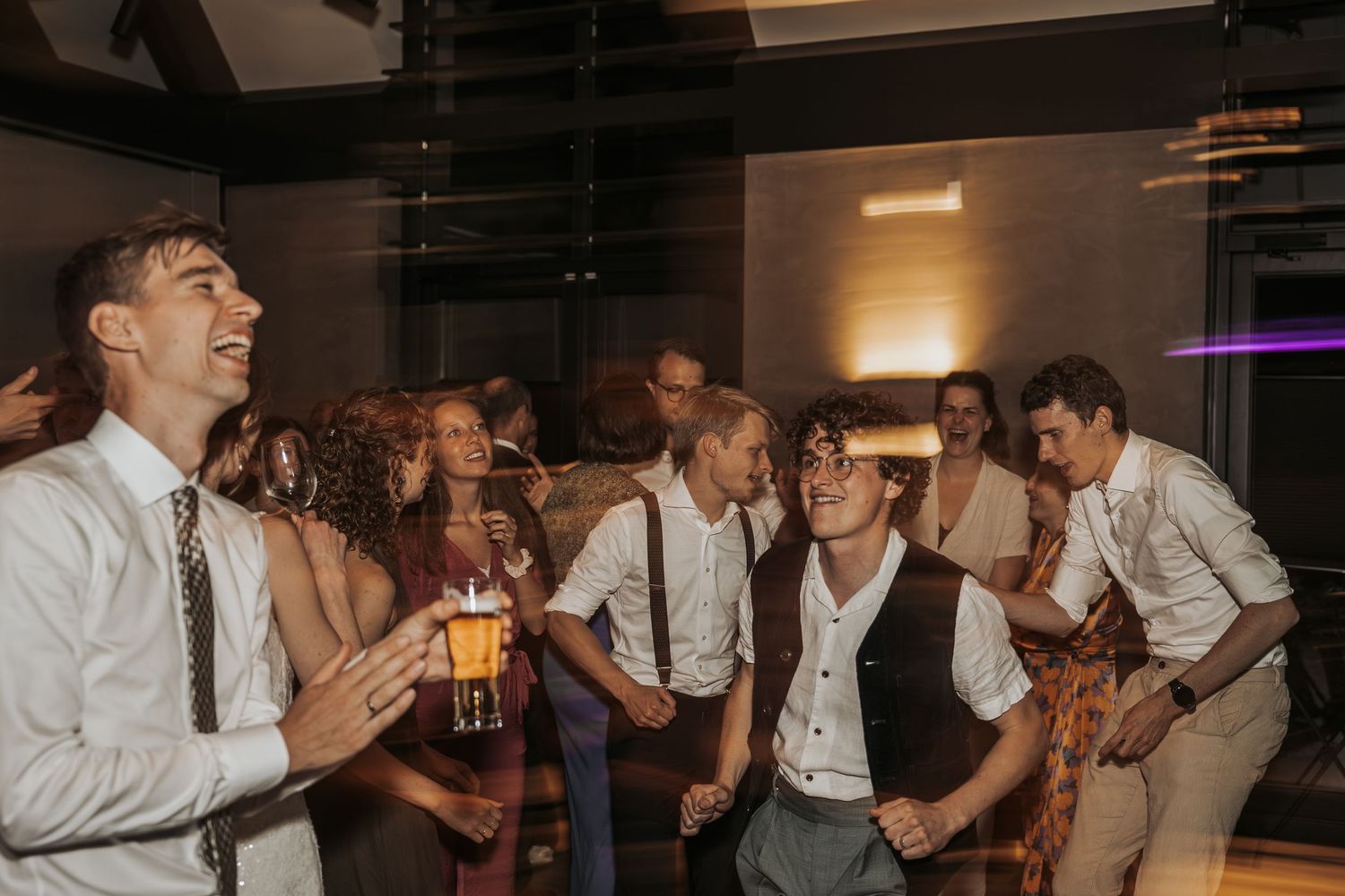 Joyful wedding guests dancing and laughing together at a lively indoor wedding reception party.