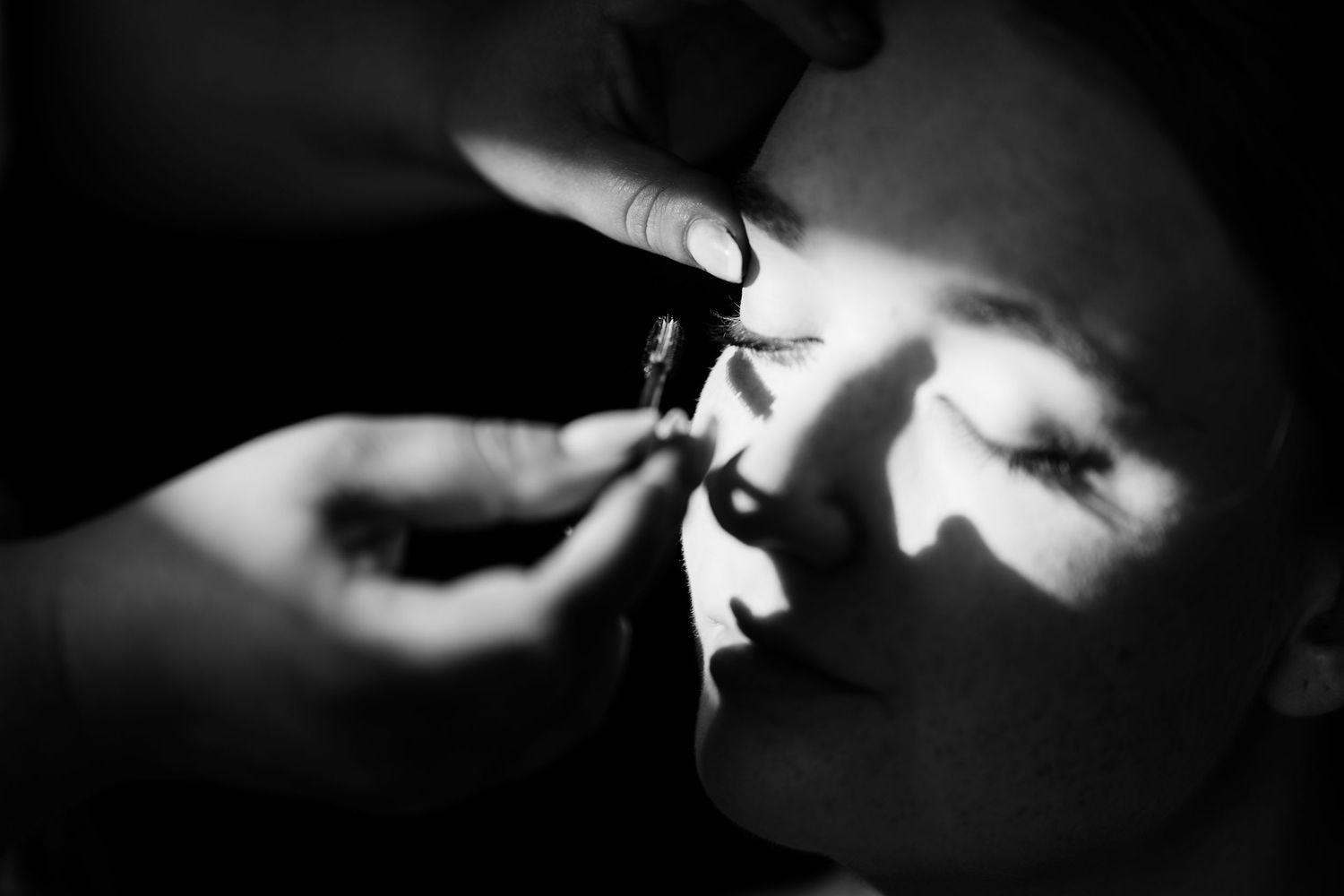 Black and white close-up of makeup artist applying eye makeup to a bride before her wedding.