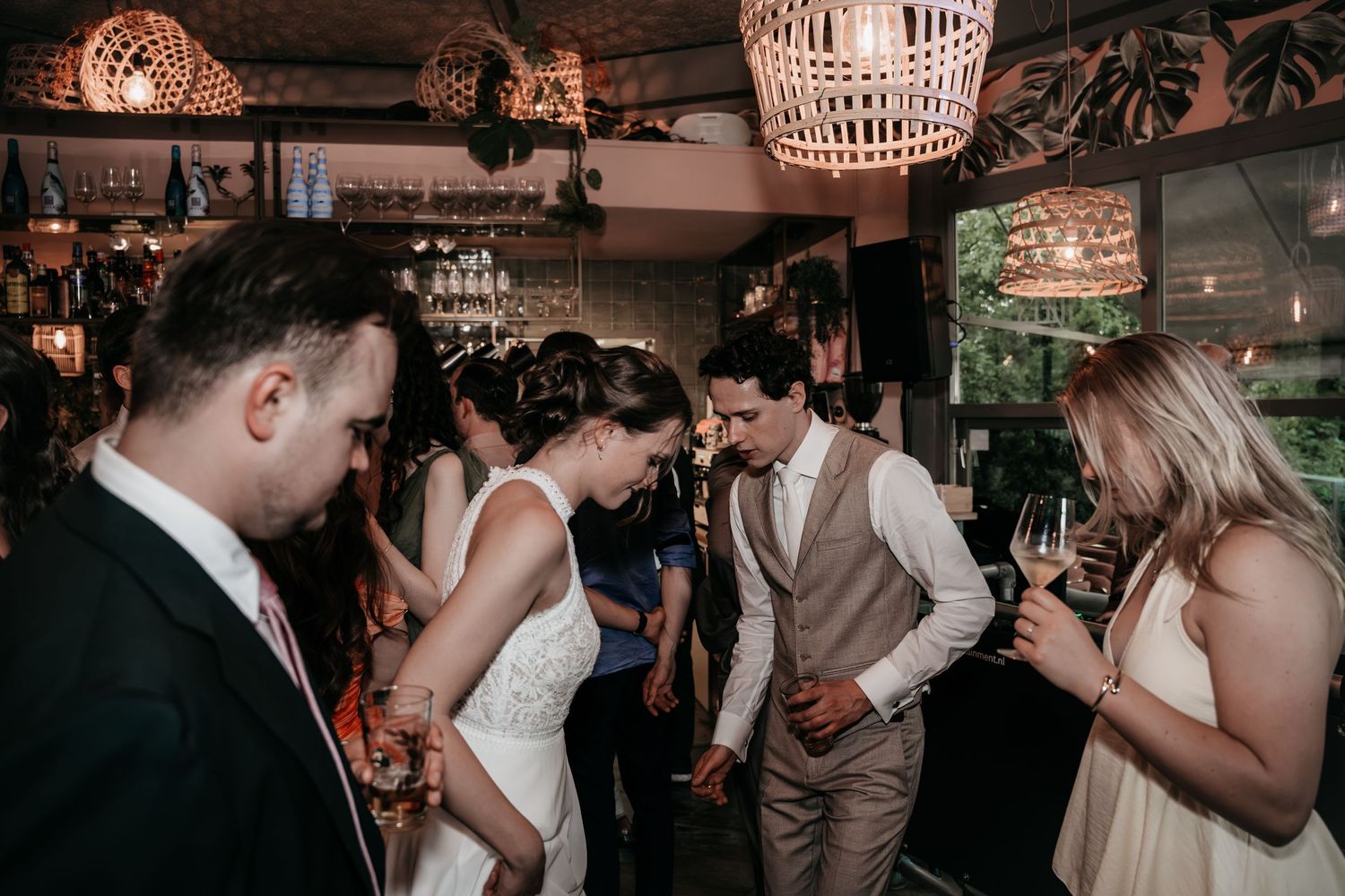 Bride and groom mingling with wedding guests near bar area at indoor tropical-themed reception.