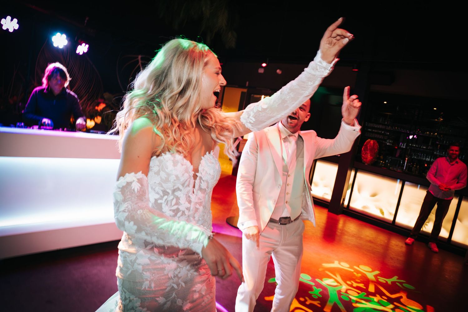 Bride and groom dancing energetically on a colorful lit dance floor at their wedding reception.