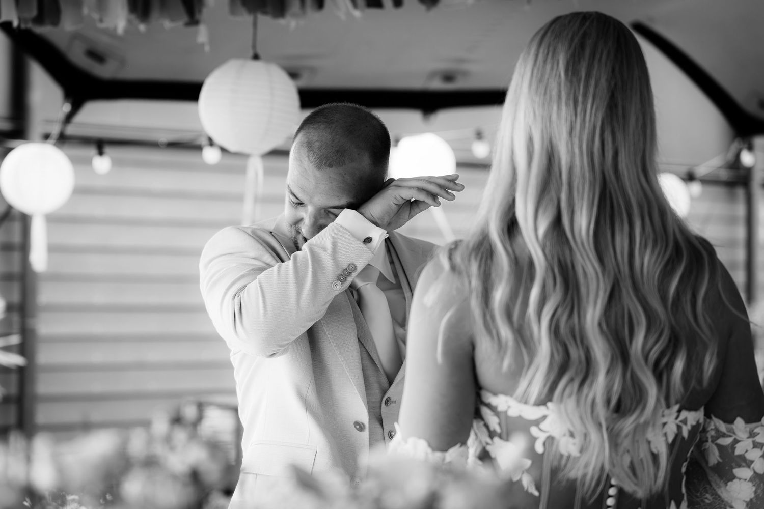 Emotional black and white photo of groom wiping tears during first dance with blonde bride.