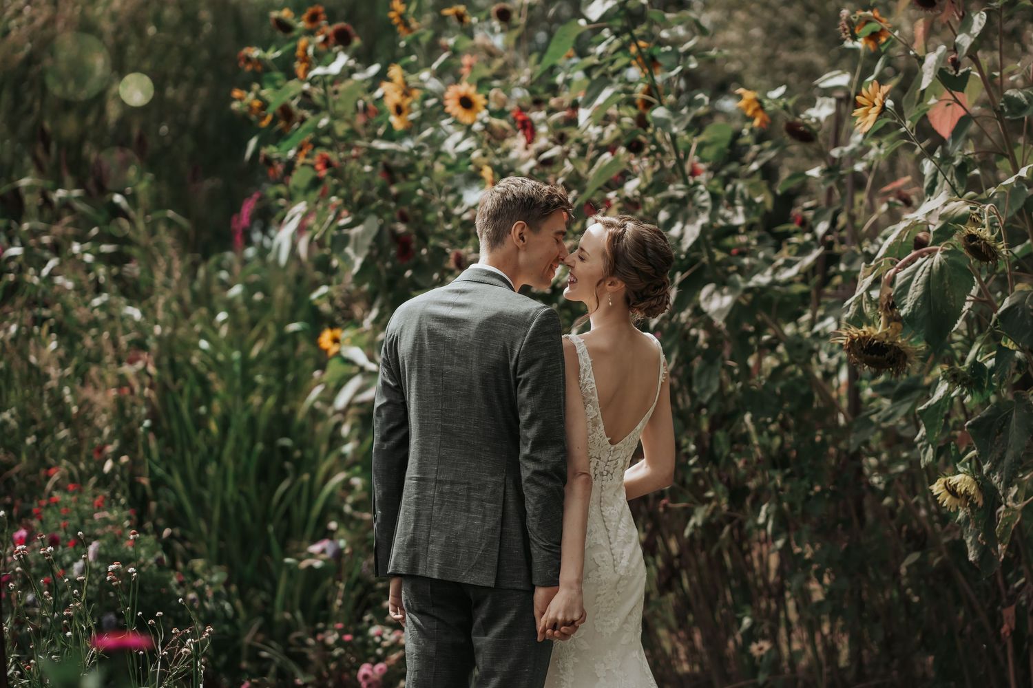 Bride and groom sharing romantic kiss surrounded by sunflowers and wildflowers in garden.