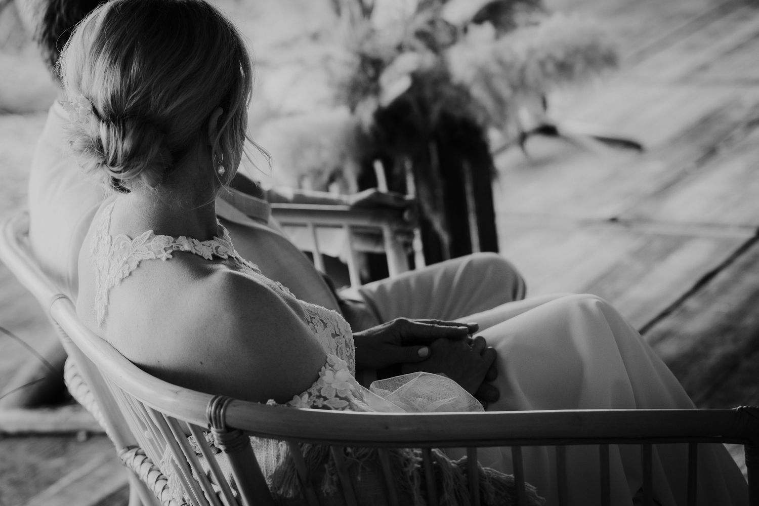Black and white photo of a bride in lace dress sitting in a chair at a wedding.