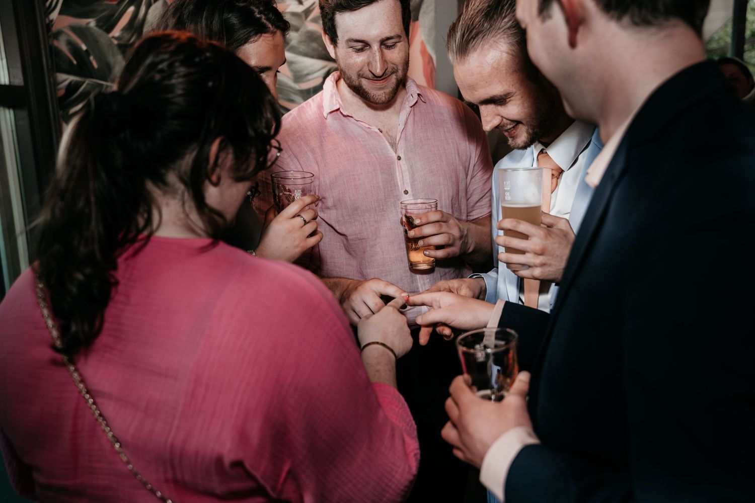 Group of wedding guests gathered closely sharing drinks and laughter at a wedding celebration.