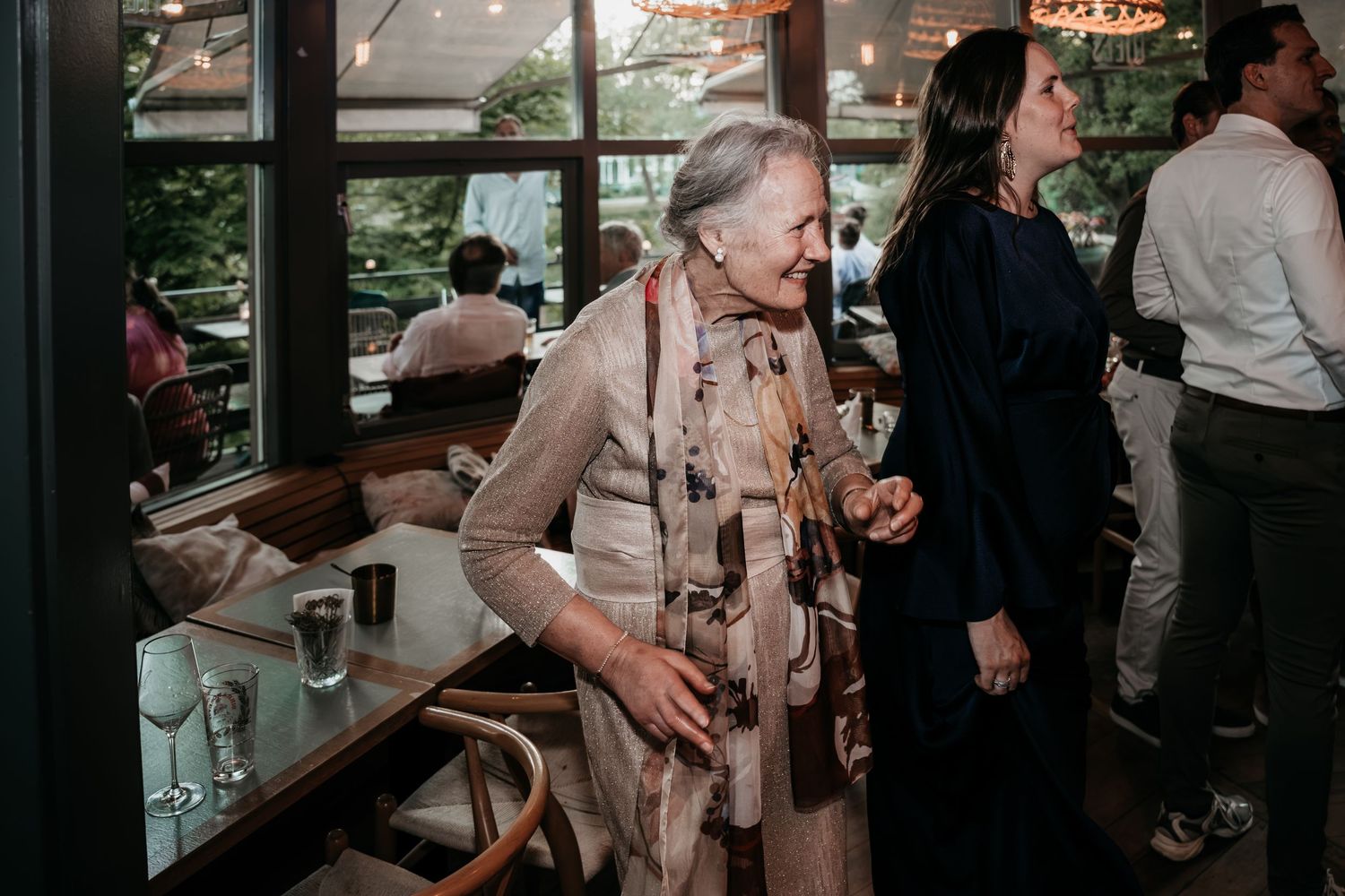 Senior female wedding guest standing by window table at sophisticated restaurant wedding reception.