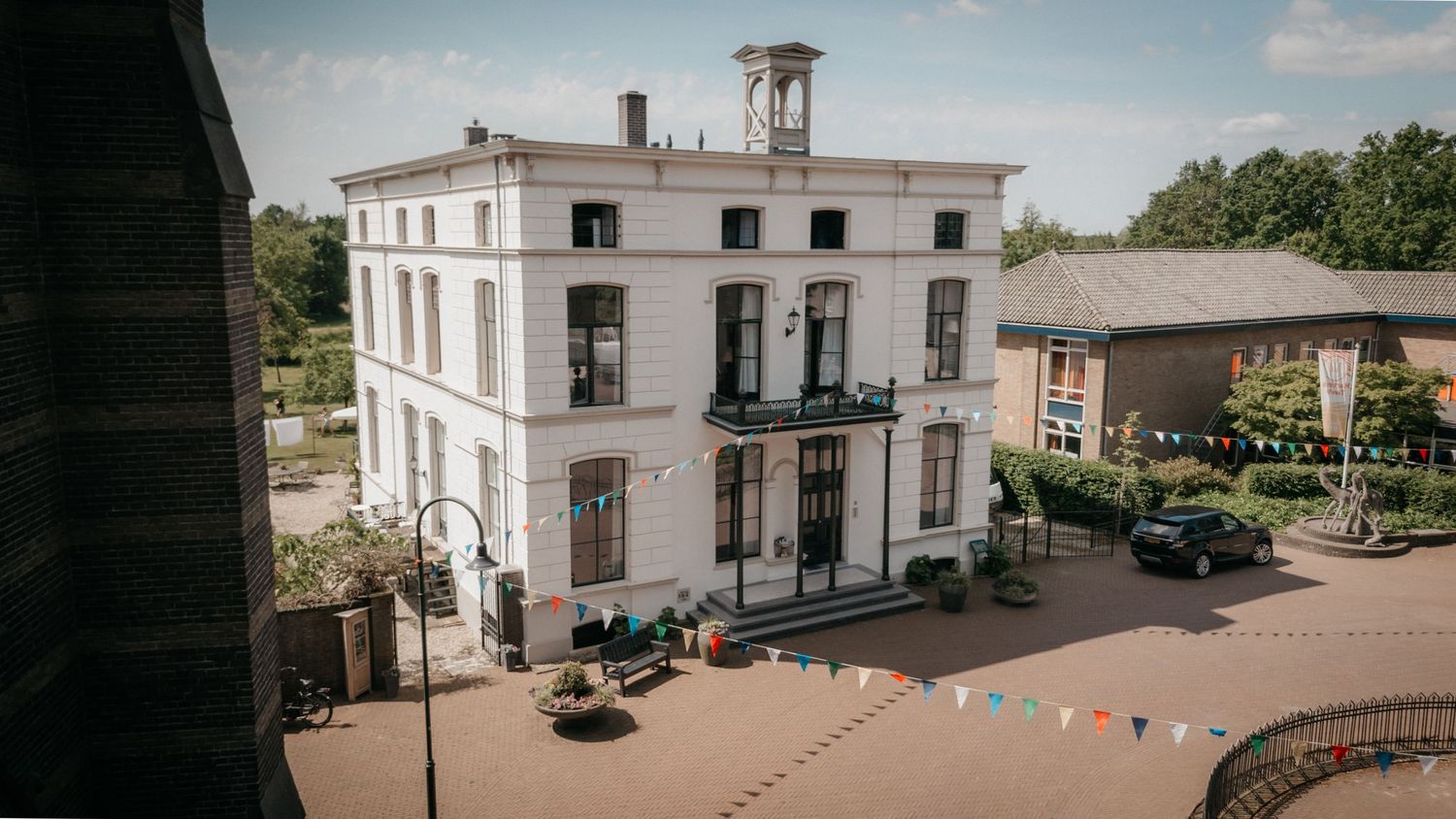 Elegant white historic manor building with decorative bunting in a charming town square setting.