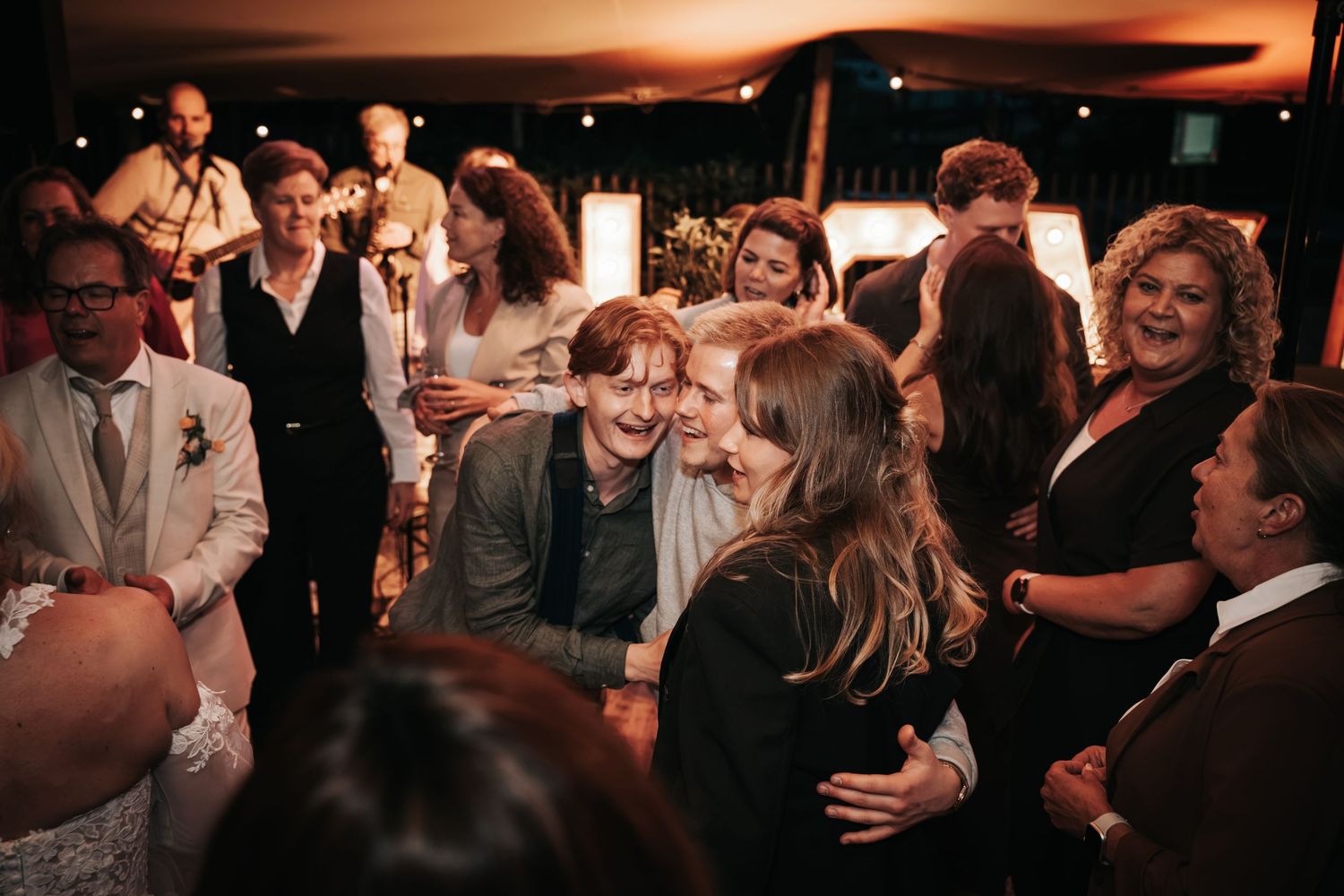 Wedding guests sharing warm embraces and smiles in a softly lit reception venue.