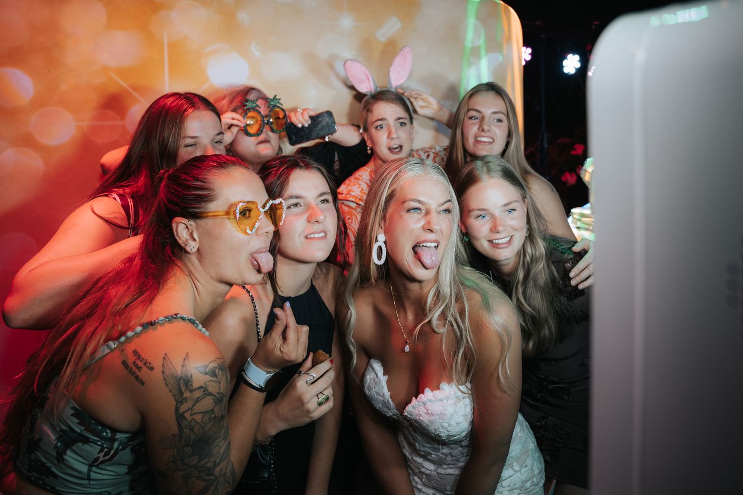 Bride and bridesmaids laughing and posing together at a fun wedding photo booth with accessories.
