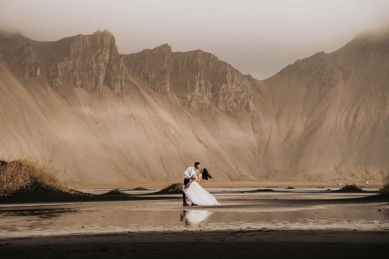 Wedding couple dancing on a black sand beach with dramatic misty mountains in the background.