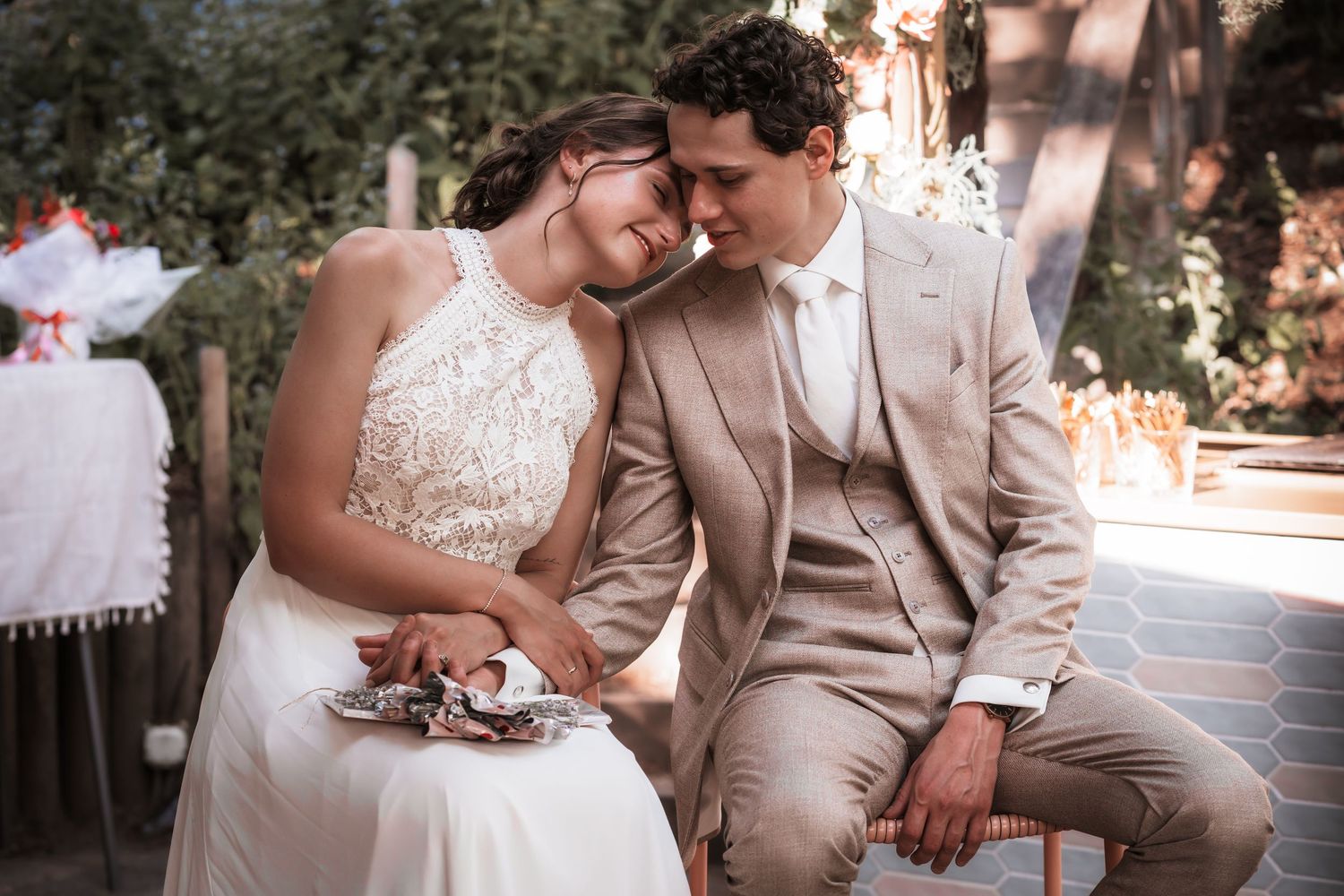Bride and groom sitting closely together outdoors, sharing an intimate moment at their wedding reception.