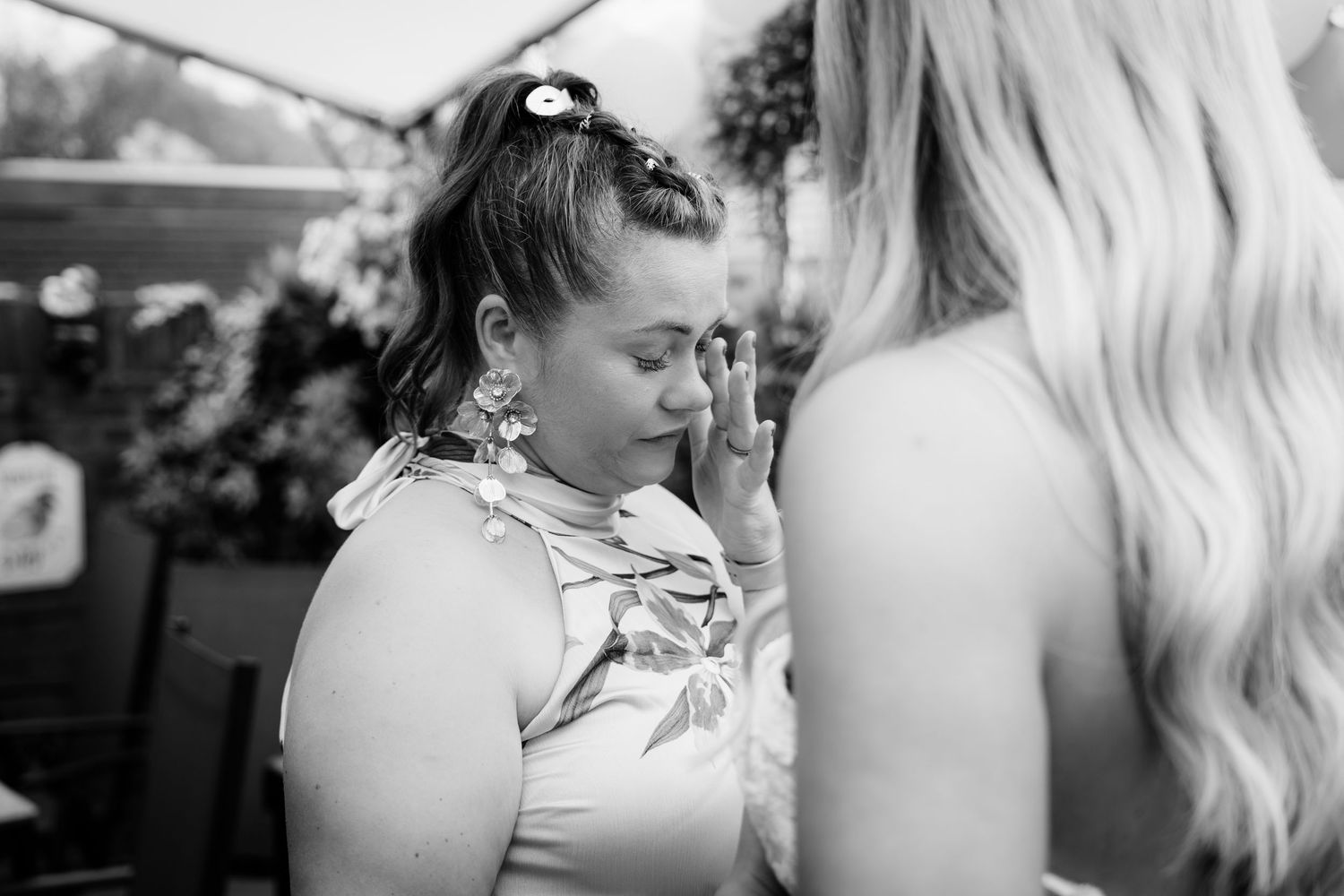 Black and white photo of emotional bridesmaid wiping tears at outdoor wedding celebration.