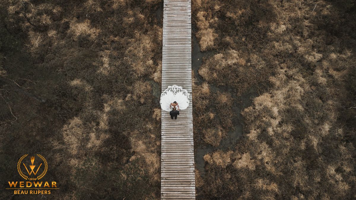 Aerial view of a couple on a wooden boardwalk path surrounded by brown fields, captured by WedWar photography.