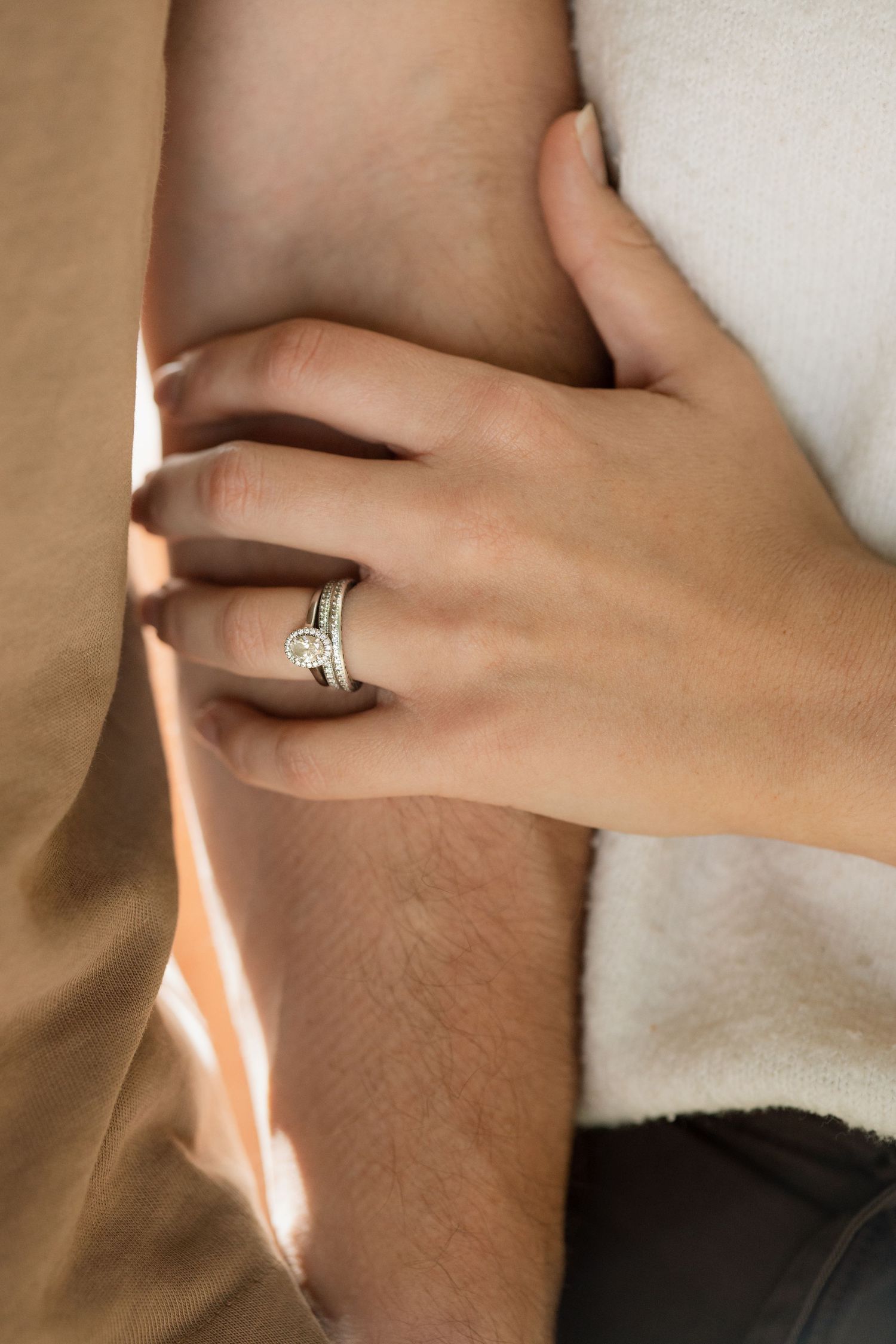 Wife holds on to husbands arm during loving photoshoot in Winchester showing her engagement and wedding rings