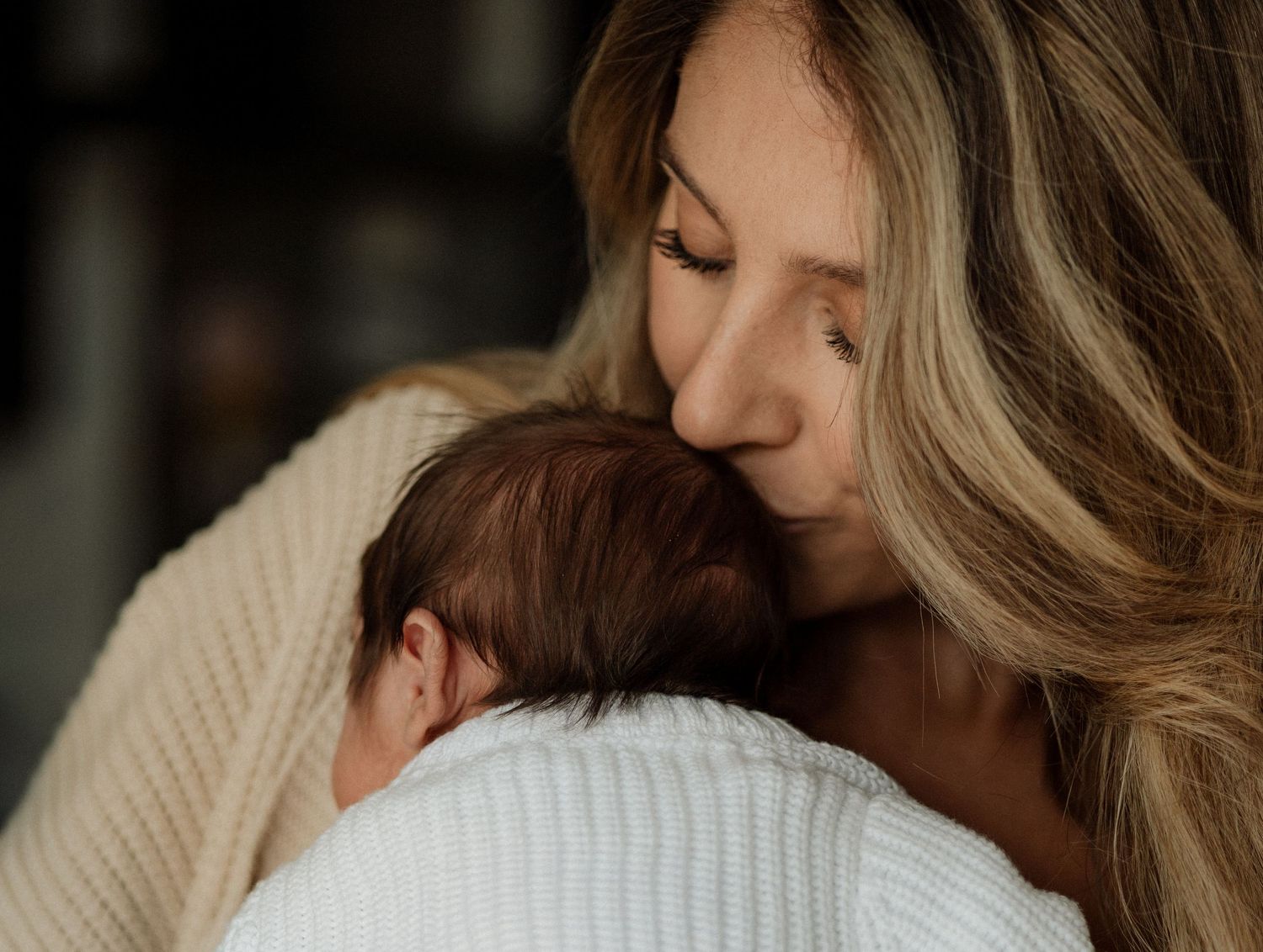 a Mum kisses a newborn babies head during an at home newborn photo session in Hampshire