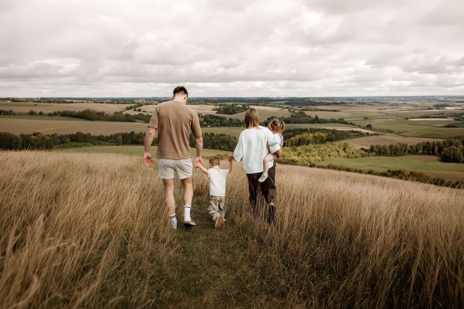 Family walk away in the long grass with stunning view on Winchester in the background on a family photoshoot in Winchester