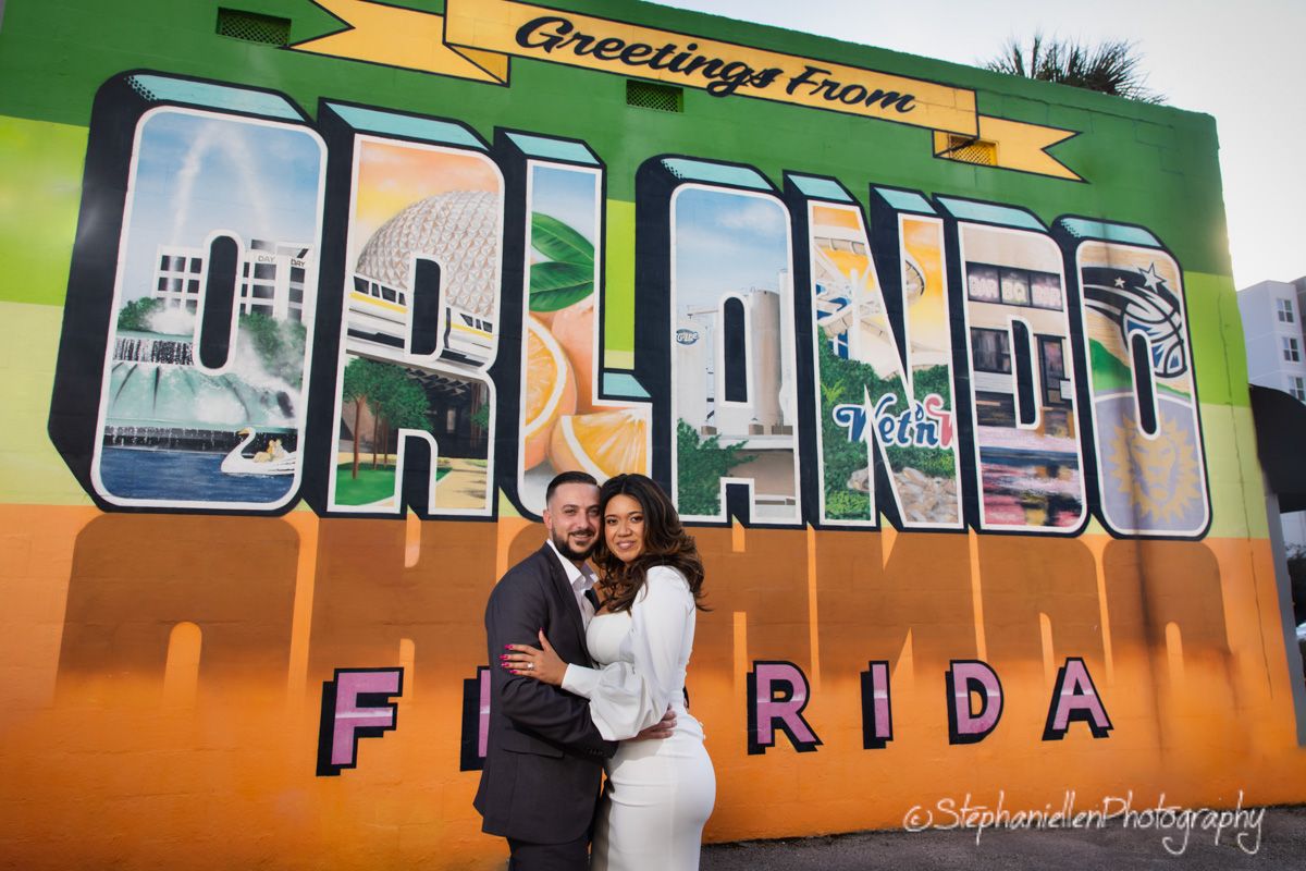 Happy couple embracing in front of colorful Greetings from Orlando Florida mural.