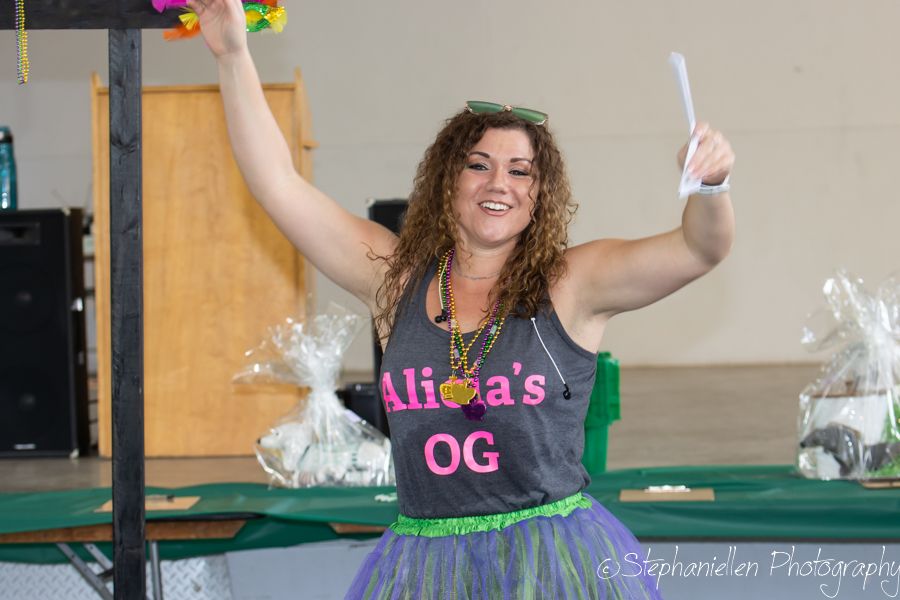 Woman in gray tank top and green tutu raises arms joyfully at a festive indoor event.